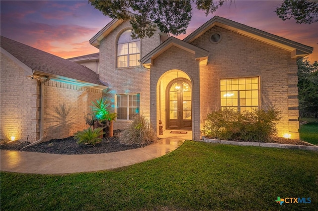 view of front of house with french doors, brick siding, and a front lawn