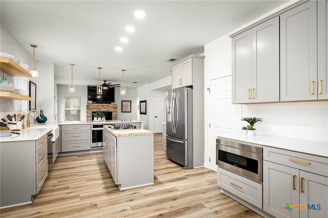 kitchen with light wood finished floors, a kitchen island, light countertops, gray cabinets, and appliances with stainless steel finishes