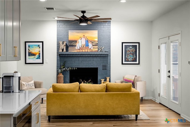 living area featuring visible vents, light wood-style flooring, a ceiling fan, recessed lighting, and a brick fireplace