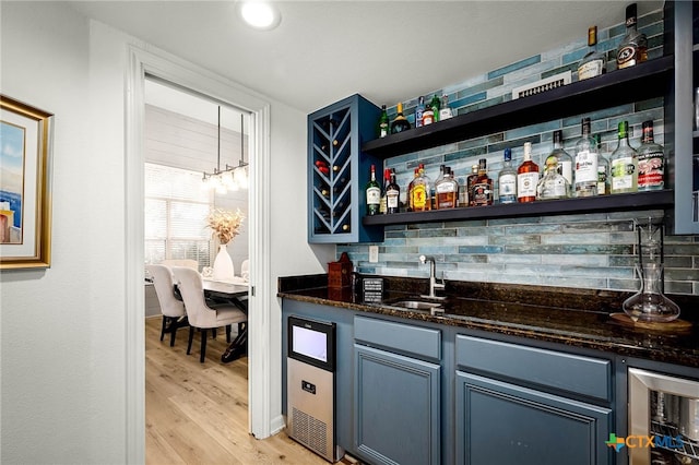 bar featuring light wood finished floors, a sink, indoor wet bar, wine cooler, and backsplash