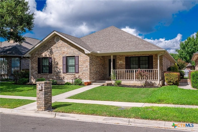 single story home featuring covered porch, a shingled roof, a front lawn, and brick siding