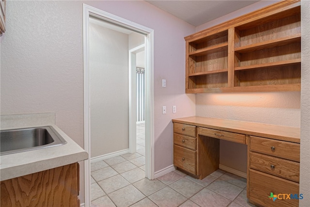 unfurnished office featuring built in desk, sink, and light tile patterned floors