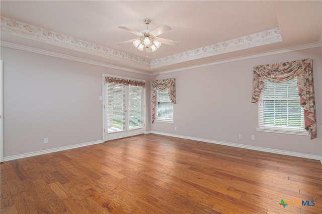 unfurnished room featuring a wealth of natural light, hardwood / wood-style flooring, ceiling fan, and a raised ceiling