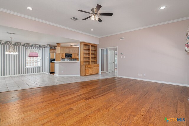 unfurnished living room featuring built in shelves, light wood-type flooring, ceiling fan with notable chandelier, and crown molding