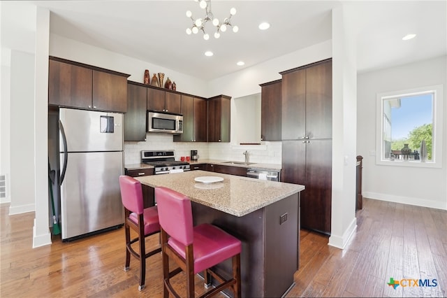 5401 Joe Sayers Ave Unit B, Austin, TX 78756 - kitchen with stainless steel appliances, dark brown cabinetry, a kitchen island, tasteful backsplash, and light wood-type flooring