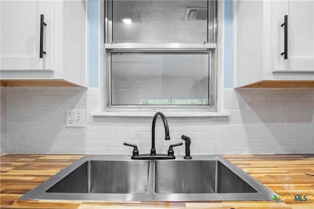 kitchen featuring butcher block counters, sink, white cabinetry, and tasteful backsplash