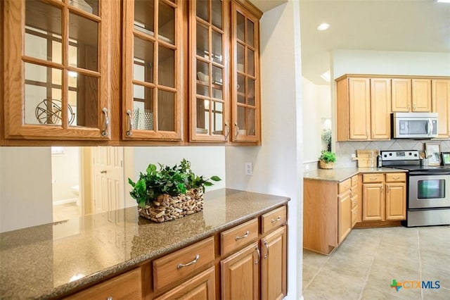 kitchen featuring appliances with stainless steel finishes, stone countertops, glass insert cabinets, and decorative backsplash