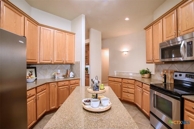 kitchen with light tile patterned floors, appliances with stainless steel finishes, light stone counters, and tasteful backsplash