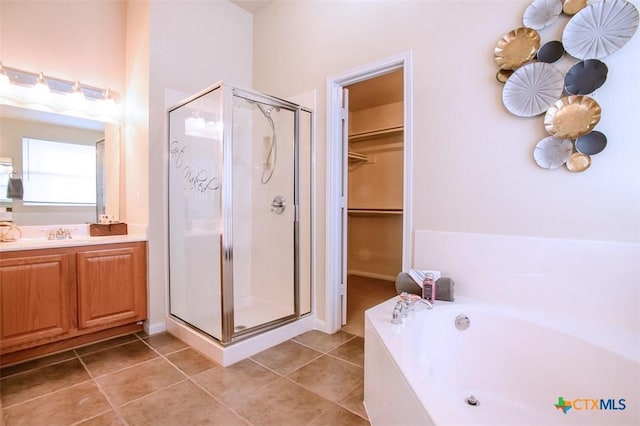 bathroom with a walk in closet, tile patterned flooring, a garden tub, and a shower stall