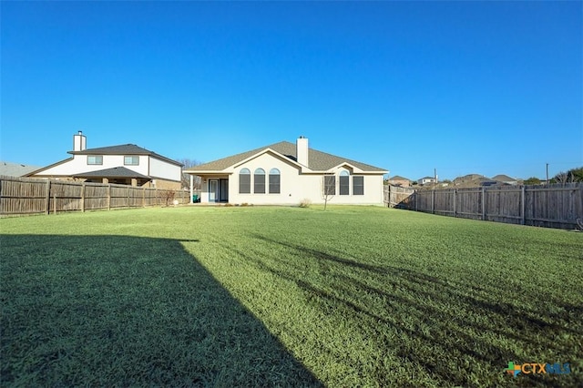 back of house with a fenced backyard, a lawn, a chimney, and stucco siding