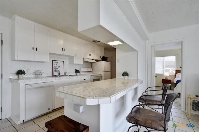 284 Lake Frst, Canyon Lake, TX 78133 - kitchen with white appliances, under cabinet range hood, tile countertops, light tile patterned floors, and white cabinetry