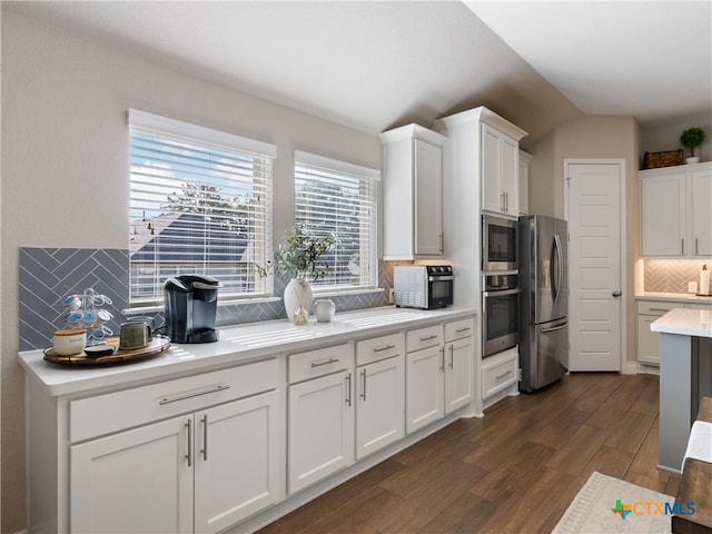 kitchen featuring appliances with stainless steel finishes, dark hardwood / wood-style flooring, tasteful backsplash, vaulted ceiling, and white cabinetry