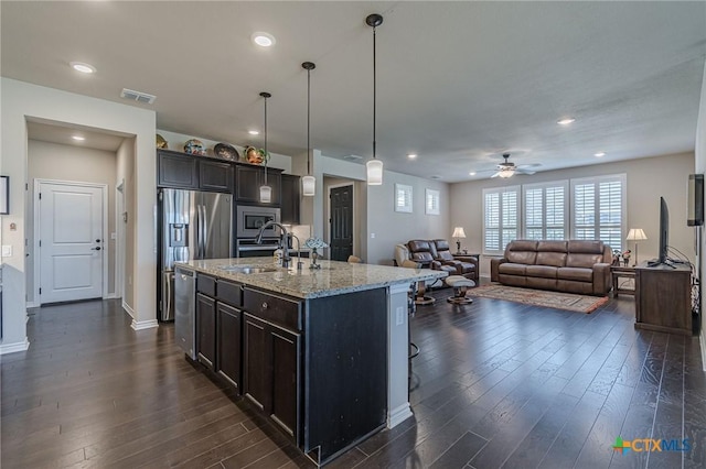 kitchen with sink, stainless steel appliances, light stone counters, a center island with sink, and decorative light fixtures