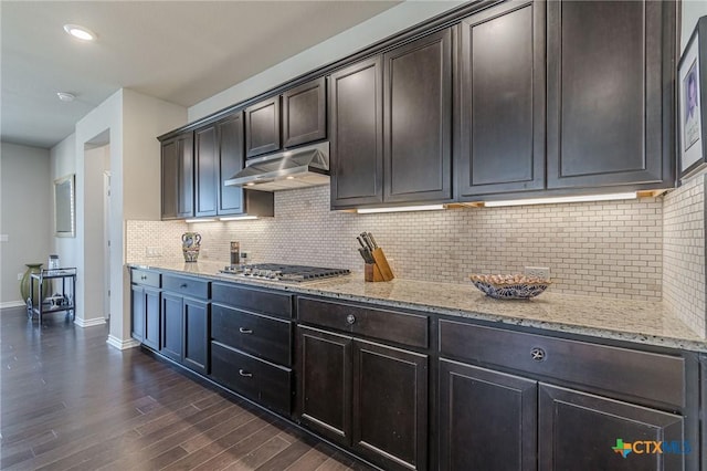 kitchen featuring under cabinet range hood, dark wood-type flooring, baseboards, light stone countertops, and stainless steel gas stovetop