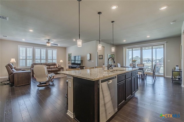 kitchen featuring light stone counters, dark hardwood / wood-style flooring, dishwasher, pendant lighting, and a kitchen island with sink