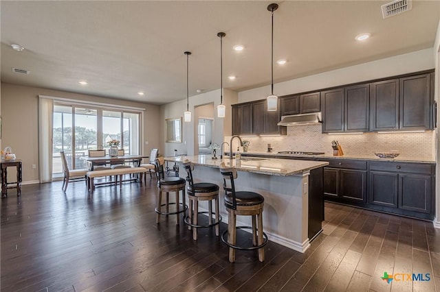 kitchen with visible vents, dark wood finished floors, a sink, under cabinet range hood, and backsplash