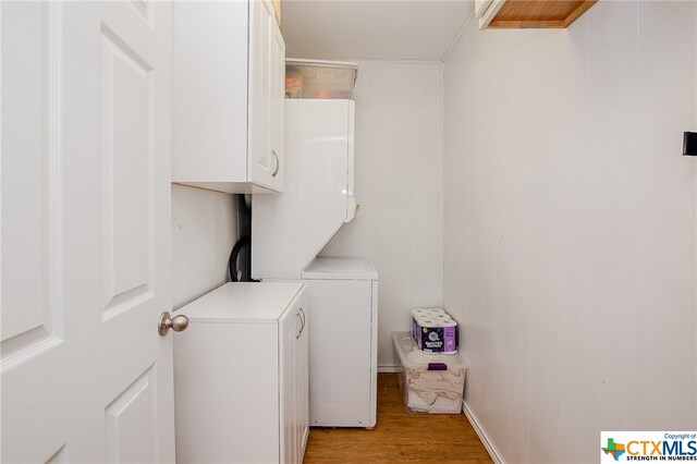 clothes washing area with light wood-style flooring, cabinet space, and stacked washer / drying machine