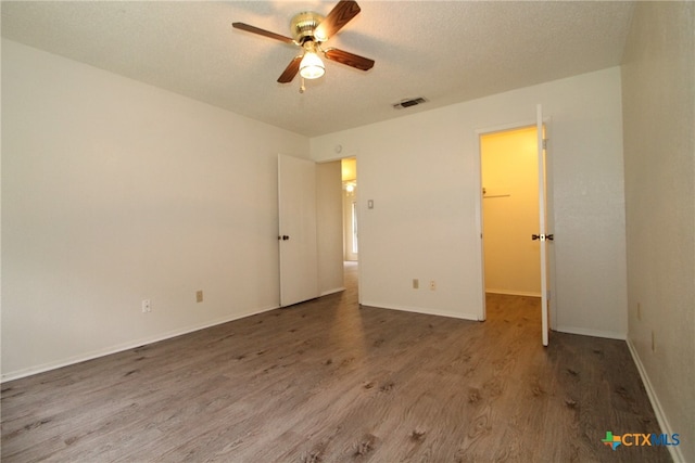 unfurnished bedroom with a textured ceiling, ceiling fan, a spacious closet, hardwood / wood-style floors, and a closet