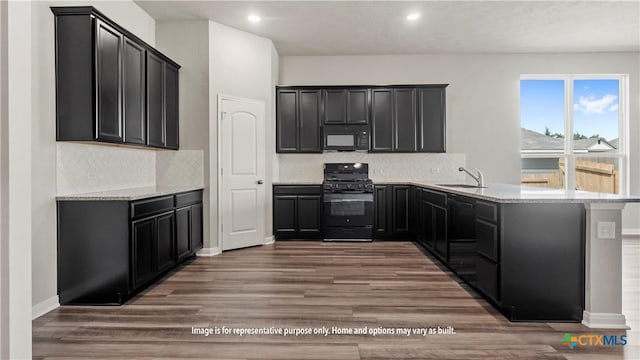 kitchen featuring black appliances, dark cabinetry, a sink, and wood finished floors