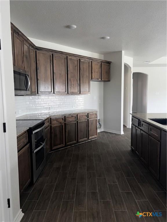 806 Dred Roger Cir, Killeen, TX 76542 - kitchen featuring stainless steel appliances, arched walkways, dark wood-style flooring, backsplash, and a textured ceiling