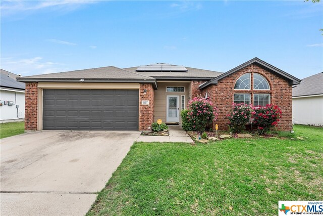 view of front of property featuring a garage, solar panels, and a front yard