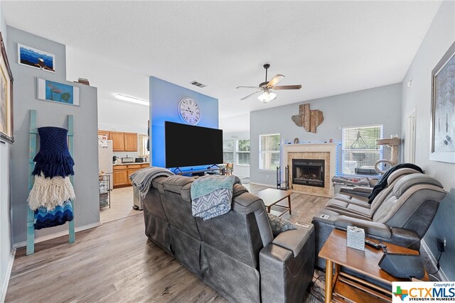 living room featuring light wood-type flooring, ceiling fan, and a fireplace