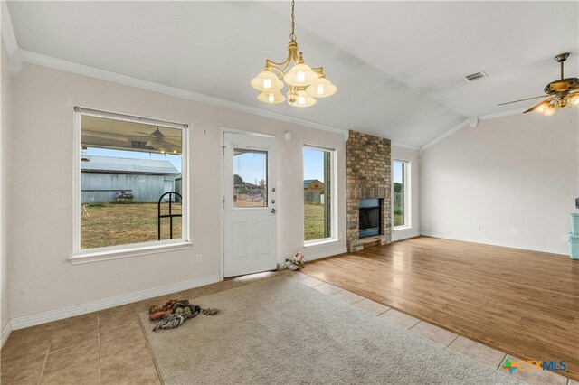 unfurnished living room featuring lofted ceiling, crown molding, light tile patterned flooring, a brick fireplace, and ceiling fan with notable chandelier