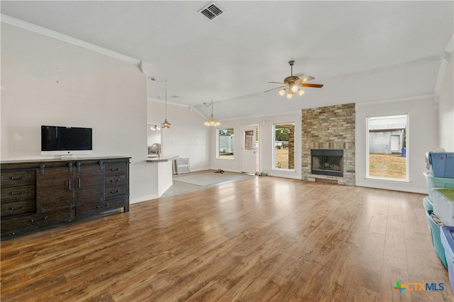 unfurnished living room with ceiling fan, a stone fireplace, light wood-type flooring, and crown molding