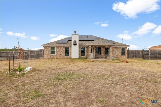 rear view of house with a lawn, a patio area, and solar panels