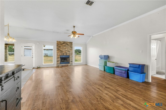 unfurnished living room with crown molding, a stone fireplace, vaulted ceiling, hardwood / wood-style flooring, and ceiling fan with notable chandelier