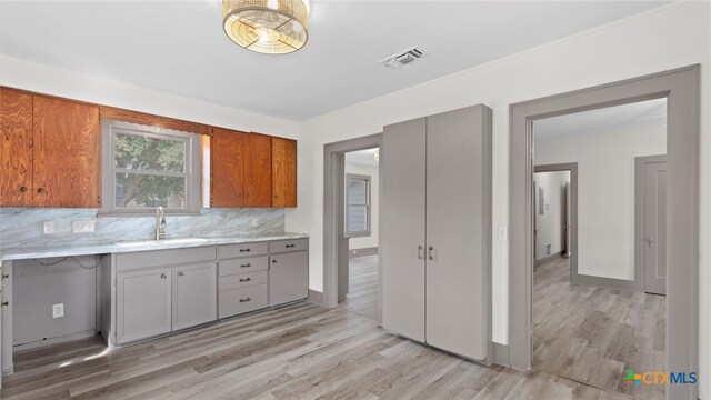 kitchen featuring backsplash, gray cabinetry, light wood-type flooring, and sink