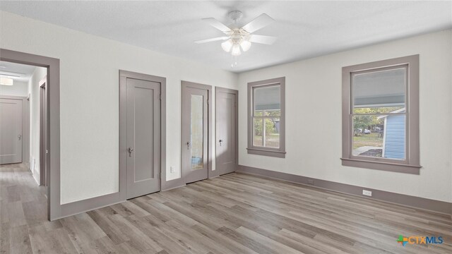 unfurnished bedroom with ceiling fan, multiple closets, light wood-type flooring, and multiple windows