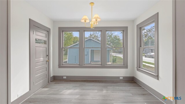 unfurnished dining area with a notable chandelier, light hardwood / wood-style floors, and a wealth of natural light