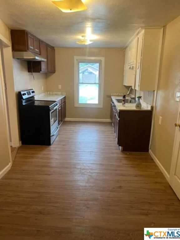 kitchen featuring under cabinet range hood, stainless steel range with electric stovetop, wood finished floors, and light countertops