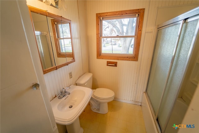 full bathroom with sink, wooden walls, shower / bath combination with glass door, and toilet