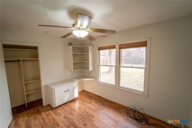 unfurnished bedroom featuring ceiling fan, a closet, built in desk, and light hardwood / wood-style flooring