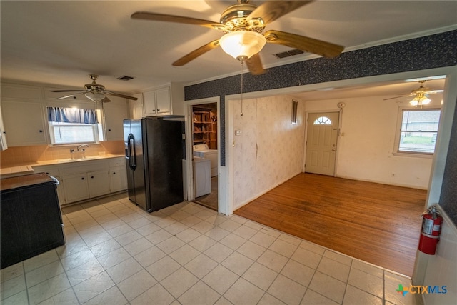 kitchen with sink, backsplash, white cabinets, black fridge, and light wood-type flooring