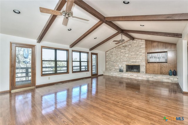 unfurnished living room with lofted ceiling with beams, ceiling fan, a stone fireplace, and light wood-type flooring