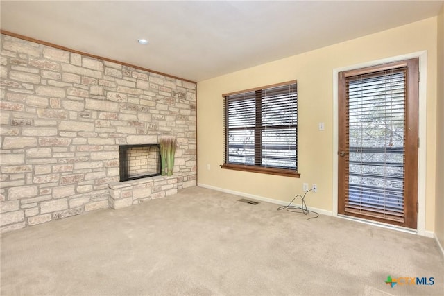 unfurnished living room with a stone fireplace, a wealth of natural light, and light colored carpet