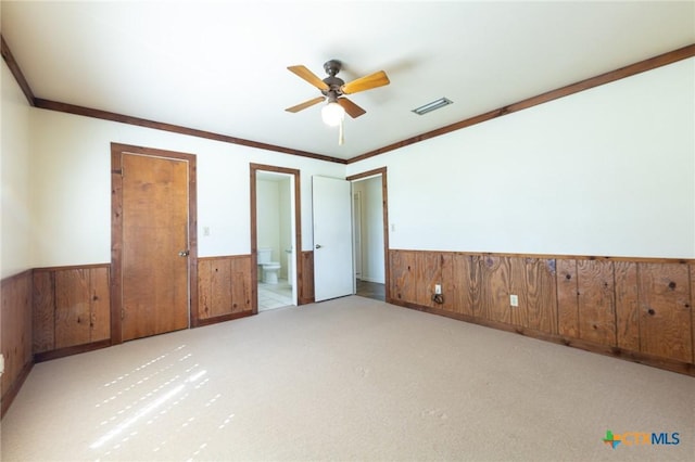 unfurnished bedroom with wooden walls, carpet floors, visible vents, ornamental molding, and wainscoting