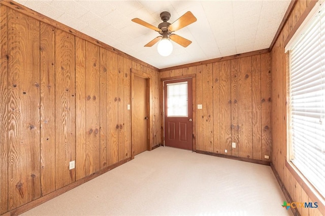 unfurnished room featuring wooden walls, baseboards, ceiling fan, ornamental molding, and carpet