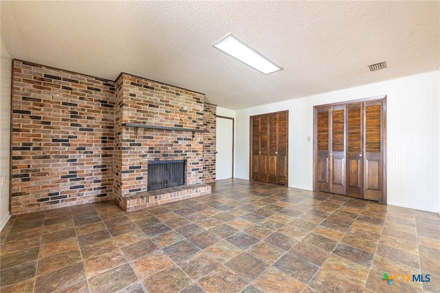 unfurnished living room featuring stone finish floor, a fireplace, visible vents, and a textured ceiling