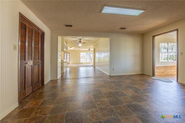 spare room with baseboards, visible vents, a ceiling fan, stone finish floor, and a textured ceiling