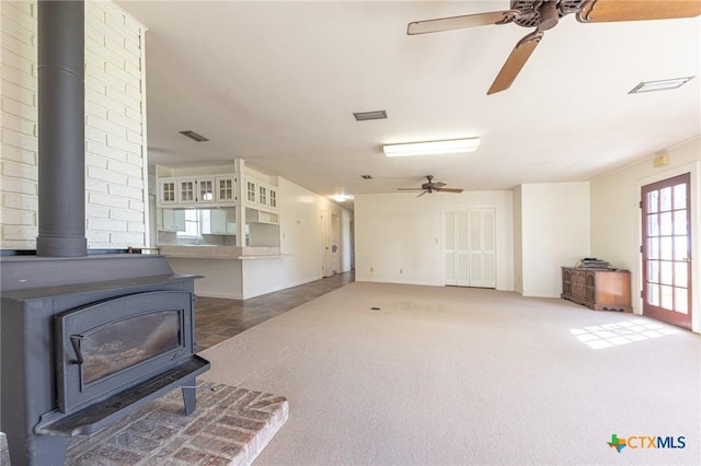 carpeted living room featuring a ceiling fan, a wood stove, and visible vents