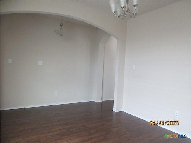 empty room featuring dark wood-style flooring, baseboards, a notable chandelier, and arched walkways