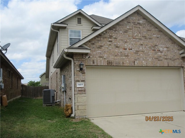 traditional-style house featuring concrete driveway, central air condition unit, an attached garage, fence, and a front lawn