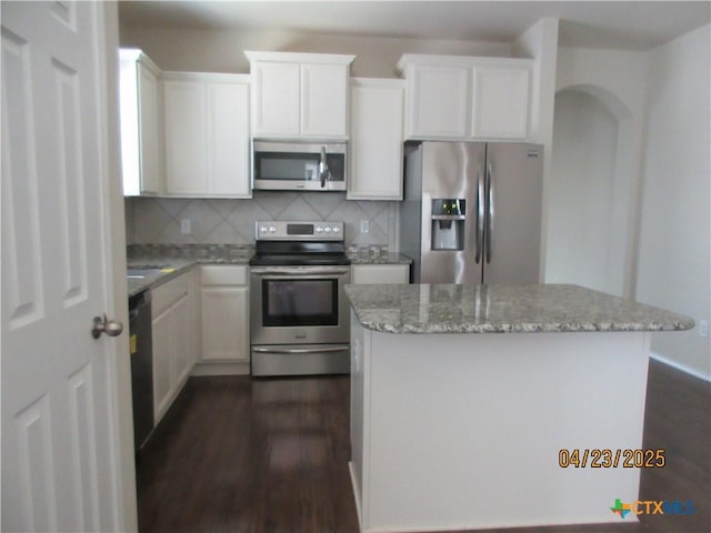 kitchen featuring stainless steel appliances, white cabinets, backsplash, dark wood-style floors, and a center island