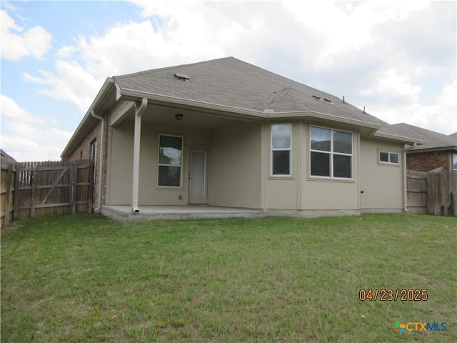 back of house with roof with shingles, a fenced backyard, a yard, and a patio area