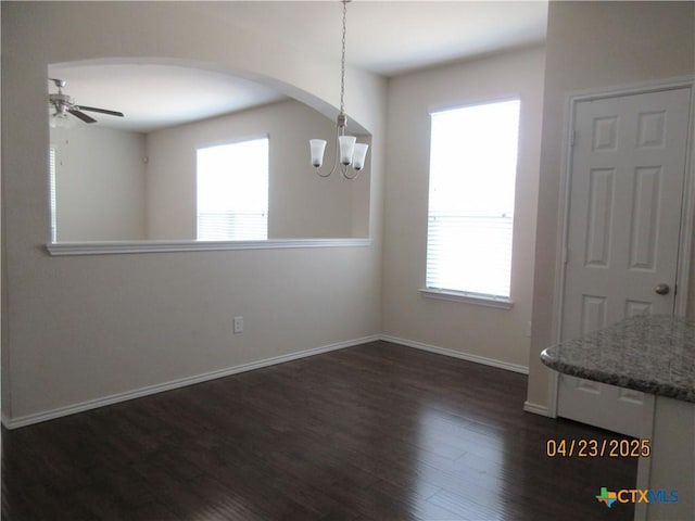 unfurnished dining area featuring dark wood-style floors, baseboards, arched walkways, and ceiling fan with notable chandelier