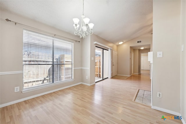 empty room with a wealth of natural light, a chandelier, light wood-type flooring, and lofted ceiling